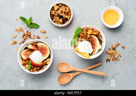 Feigen mit Joghurt und Honig und Haferflocken Müsli auf grauem Beton Hintergrund. Tabelle Ansicht von oben. Gesunde Ernährung Stockfoto