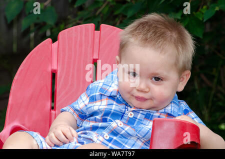 Baby boy in einem roten Stuhl, ein lustiges Gesicht Stockfoto