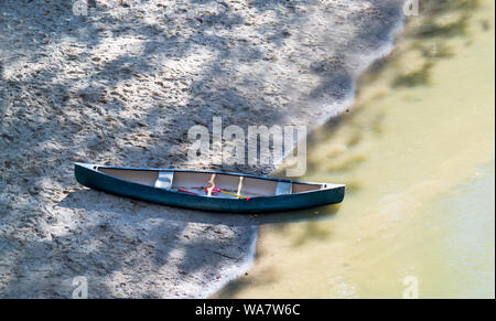 Eine grüne Kanu sitzt die Hälfte am Sandstrand und teilweise in der ... Stockfoto