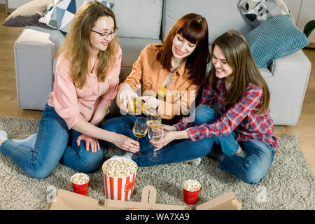 Freundschaft, Essen und Freizeitaktivitäten Konzept - glücklich drei weibliche Freunde essen Pizza, Popcorn und trinken Wein zu Hause in Abend. Stockfoto