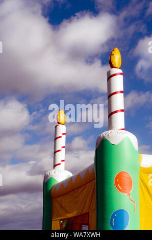 Große aufblasbare Geburtstag Kerzen stehen in einem bewölkten Himmel, ruht auf einem bunten Hüpfburgen Haus bei einem Kind Geburtstag Stockfoto