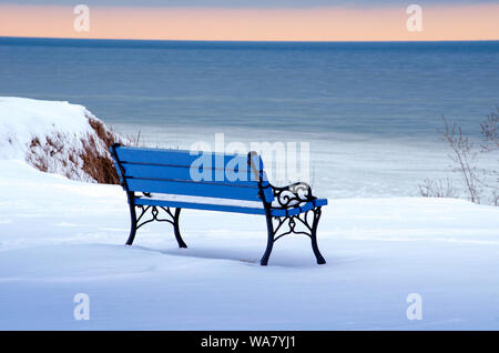 Eine kalte Leere blaue Parkbank über sieht eine Icy Lake Michigan in den Farben Weiß und Blau. Stockfoto