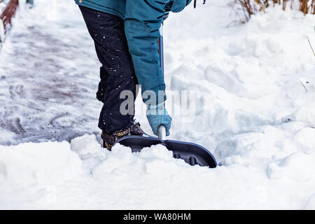 Ein Mann reinigt den Schnee in der Nähe des Hauses mit einer großen schwarzen Schaufel. Stockfoto