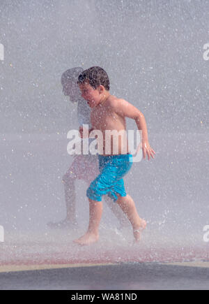 Zwei Jungen Rennen durch einen Splash pad Brunnen, man mögen ein Schatten der anderen Stockfoto
