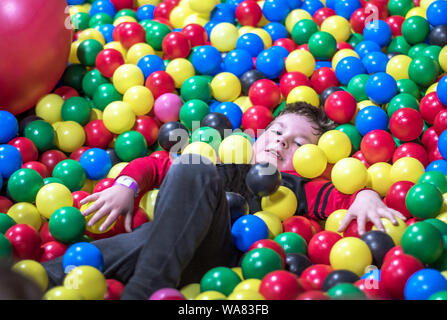 Ein kleiner Junge liegt teilweise in einem großen Haufen aus Kunststoff, bunten Bällen begraben Stockfoto