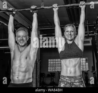 Ein attraktives Paar mittleren Alters zusammen tut, ein Fitness Training und Spaß haben. Athletische älterer Mann und Frau sind hängend auf der horizontalen Leiste. Stockfoto