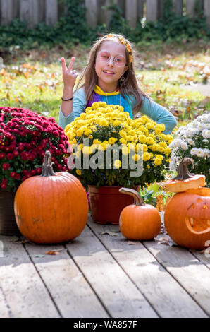Ein kleines Mädchen, gekleidet wie ein Hippie Blume Kind, blinkt ein Friedensabkommen unterzeichnen, wie sie im Kostüm wirft auf Halloween Stockfoto