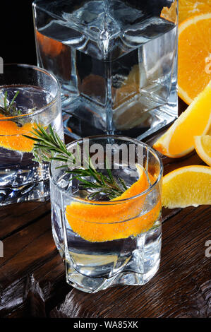 Cocktail classic Dry Gin mit Tonic und Orangenschale mit einem Zweig Rosmarin auf einem Holzbrett mit Scheiben juicy orange Stockfoto