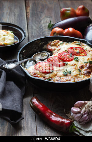 Frische hausgemachte Moussaka im Iron Skillet auf rustikalen Holzmöbeln Hintergrund mit Zutaten. Griechische Küche. Stockfoto