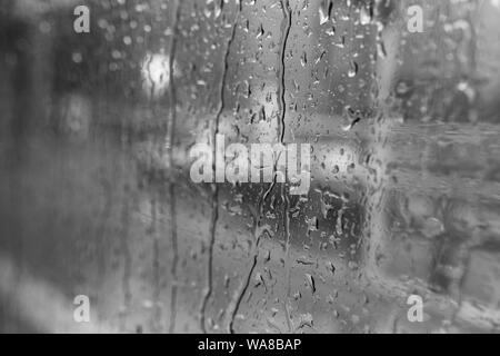 Schwarze und weiße Stimmung und Ton und Nahaufnahmen und Makro Aussicht auf regen Wassertropfen auf außen Fenster des Bus oder Zug weiß Unschärfe abstrakt Blick auf die Straße. Stockfoto