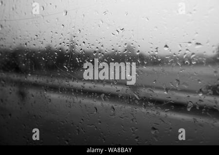 Schwarze und weiße Stimmung und Ton und Nahaufnahmen und Makro Aussicht auf regen Wassertropfen auf außen Fenster auf der Brücke und Unschärfe Hintergrund des Flusses. Stockfoto