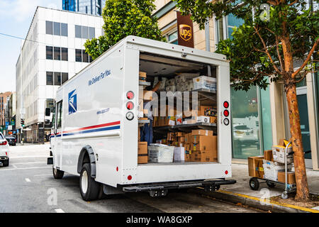 August 10, 2019 San Francisco/CA/USA - USPS delivery van vor einem UPS gestoppt, entladen Amazon Pakete Stockfoto