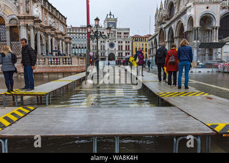 Menschen zu Fuß auf erhöhten Plattformen während der Acqua Alta (hohe Wasser) Fall, Piazzetta di San Marco, Venedig, Italien Stockfoto