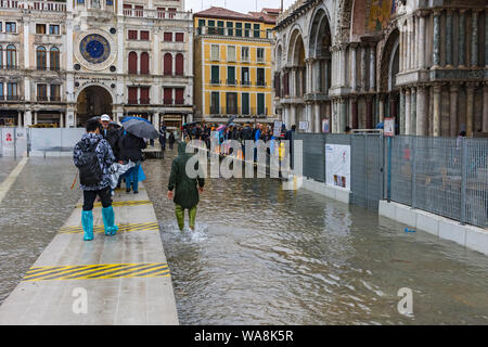 Menschen zu Fuß auf erhöhten Plattformen während der Acqua Alta (hohe Wasser) Fall, vor der Basilika di San Marco, Saint Mark's Square, Venedig, Italien Stockfoto