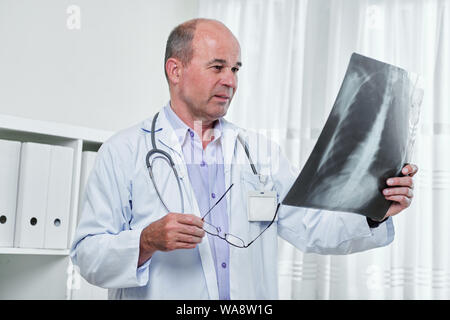 Ernsthafte kaukasischen Radiologen, die Gläser und das Betrachten der Lunge Röntgen in seiner Hand. Stockfoto