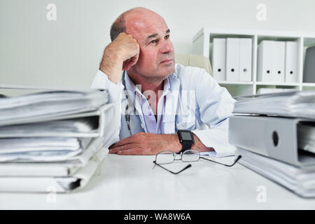 Reifen für Allgemeinmedizin an seinem Tisch sitzen mit Bindemittel und Dokumente angehäuft und Tagträumen Stockfoto