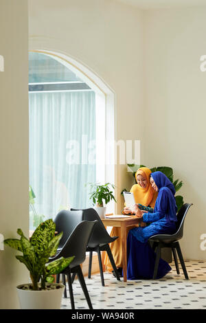 Ziemlich lächelnden jungen muslimischen Frauen im Cafe sitzen und beobachtete Fotos auf Tablet-PC Stockfoto
