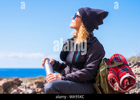 Aktive kaukasische Frau ruht sich nach einem Trekking zu Fuß - outdor Freizeitaktivitäten nutze für gesunde Menschen - Ozean. ansehen und blauen Himmel im Hintergrund - su Stockfoto