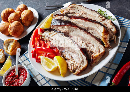 Ruckartig Schweinebauch in Scheiben geschnitten auf einer weißen Platte auf einer konkreten Tabelle mit jamaikanischen frittierte Klöße und Hot Chili Sauce, horizontale Ansicht von oben Stockfoto