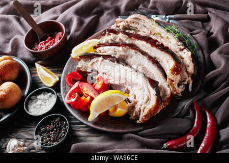 In Scheiben geschnitten, ruckartig Schweinebauch mit Zitrone Keile und Paprika auf einem Steingut Teller auf einen Holztisch mit braunen Tuch, close-up Stockfoto