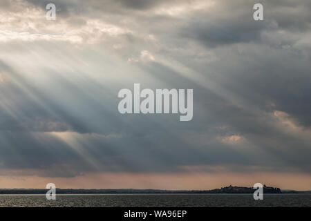 Sonnenstrahlen in der Nähe von Sonnenuntergang, mit dunklen Wolken im Hintergrund, eine orange Himmel und See Trasimeno (Umbrien, Italien) unter Stockfoto