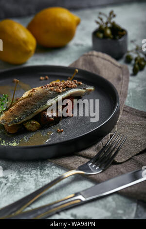 Gegrillten Wolfsbarsch mit Auberginen und Kalk. Horizontal oben anzeigen, Top Shot. Platz kopieren, grauer Beton Marmor Hintergrund, weiches Licht. Essen Fashion Foto. Stockfoto