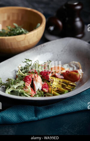 Salat mit Krabben und Avocado auf einem dunklen Hintergrund. Rucola Salat, gewürzt mit Soße auf Weißwein mit Krabben Fleisch und gegrilltem Avocado in Weichen Stockfoto