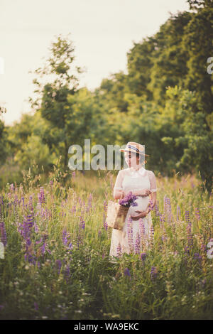 Schwangere Frau in weißem Kleid mit einem strohkorb mit Wildblumen Stockfoto