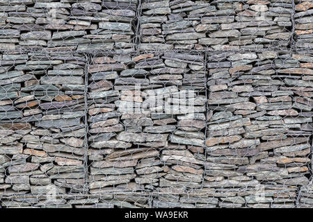 Eine Wand mit kleinen grauen Steine hinter einem Gitter aus Metall ausgekleidet, so dass die Berge bröckeln nicht. Stein Textur Stockfoto