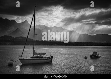 Regentropfen und zwei Boote auf Bojen am Thunersee bei Regen mit Sonnenstrahlen und Stockhorn Bergkette im Hintergrund Stockfoto