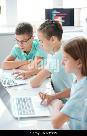 Reihe Der schwere süße schoolkids in casualwear sitzen Schreibtisch vor Laptops Stockfoto