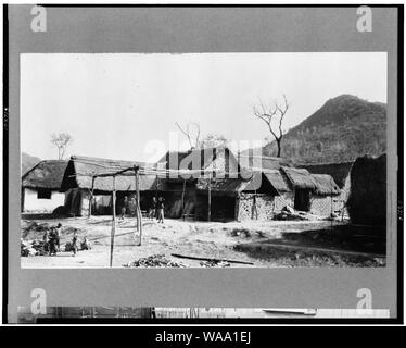 China - Mud-brick Häusern mit Strohdächern, Menschen in Hof im Vordergrund Stockfoto