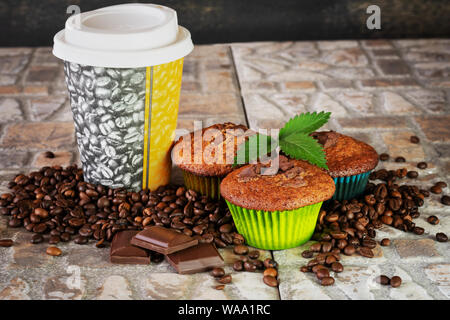 Muffins und Kaffee mit grüner Zweig zu gehen, Stücke von Schokolade und Kaffee Bohnen auf Steinzeug Hintergrund. Stockfoto