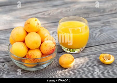 Gelbe Aprikosen in Glas Schale und Saft auf hölzernen Tisch Stockfoto