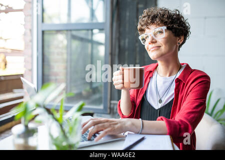 Junge zuversichtlich Geschäftsfrau mit Becher trinken Vor dem Laptop sitzen Stockfoto