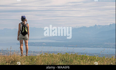 Eine einsame weibliche Wanderer steht auf einem Berg mit Blick auf die Ansicht eines großen alpinen See und die umliegenden Alpengipfel. Stockfoto