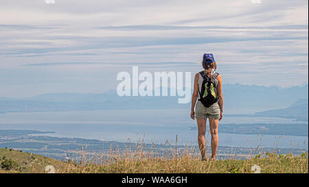 Eine einsame weibliche Wanderer steht auf einem Berg mit Blick auf die Ansicht eines großen alpinen See und die umliegenden Alpengipfel. Stockfoto