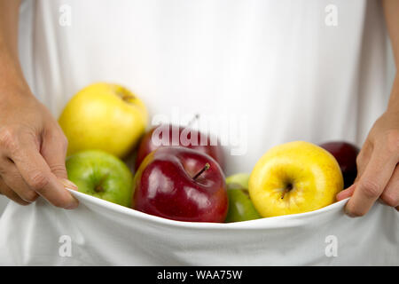 Ein kaukasischer Frau hält einige Äpfel verschiedener Arten und Farben in ihr weißes Kleid in Ihre Hände umklammerten Stockfoto