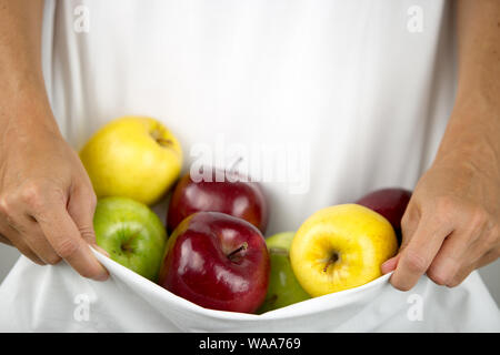 Ein kaukasischer Frau hält einige Äpfel verschiedener Arten und Farben in ihr weißes Kleid in Ihre Hände umklammerten Stockfoto