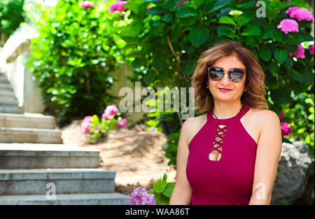 Porträt einer schönen Frau mittleren Alters mit Sonnenbrille Spaß im Freien entspannen Sie sich im Garten Stockfoto