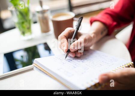Hand der jungen Geschäftsfrau mit Stift Notizen auf Seite des Notebooks Stockfoto