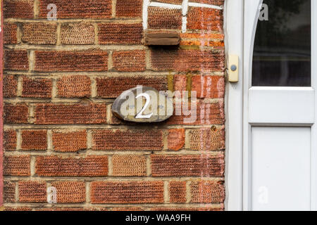 Haus Nummer zwei auf einem roten Ziegelmauer mit den 2 in Holz geschnitzten Stockfoto