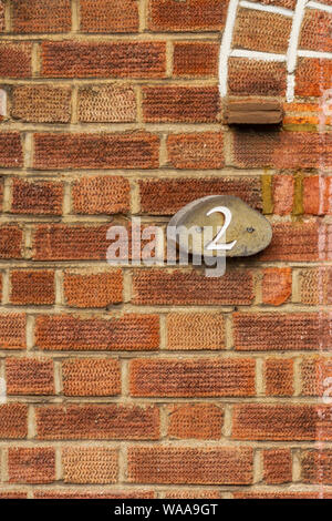 Haus Nummer zwei auf einem roten Ziegelmauer mit den 2 in Holz geschnitzten Stockfoto