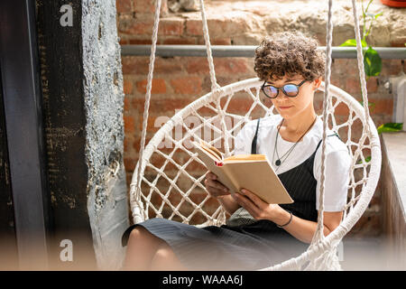 Moderne junge Frau in casualwear und Brillen Roman lesen Stockfoto