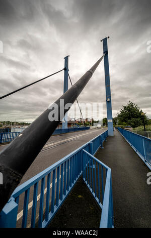 Dramatischer Blick auf eine Schaukelbrücke mit Geländer, die unter bewölktem Himmel in die Ferne führt Stockfoto