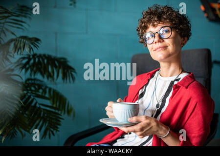 Junge serene elegante Frau mit einer Tasse Tee oder Kaffee entspannen im Cafe Stockfoto
