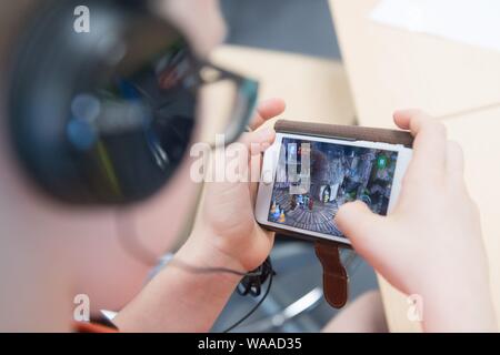 Dresden, Deutschland. 19 Aug, 2019. Ein Student sitzt am Rande einer Eröffnungsveranstaltung mit Kopfhörern in einem Klassenzimmer der Schule Universität und spielt ein Spiel auf einem Smartphone. Die öffentlichen und freien Grund- und Hauptschule ist ein gemeinsames Projekt der Landeshauptstadt Dresden und der TU Dresden. Credit: Sebastian Kahnert/dpa-Zentralbild/dpa/Alamy leben Nachrichten Stockfoto