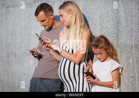 Image der jungen Eltern, Mädchen mit Handys in den Händen neben graue Betonwand außerhalb Stockfoto