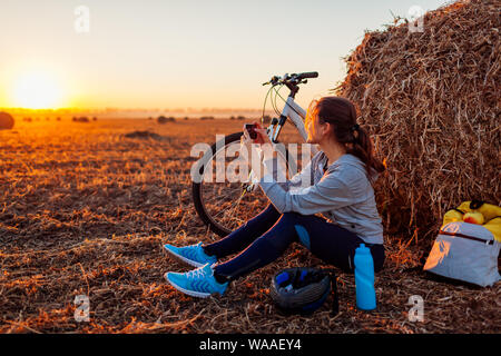 Junge Radfahrer Rest nach einer Fahrt im Herbst Feld bei Sonnenuntergang. Frau unter Bild über Telefon von haystack Stockfoto