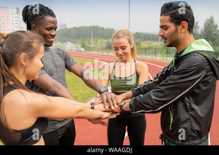 Vier junge interkulturelle Menschen in Activewear, Haufen von Händen im Freien Stockfoto